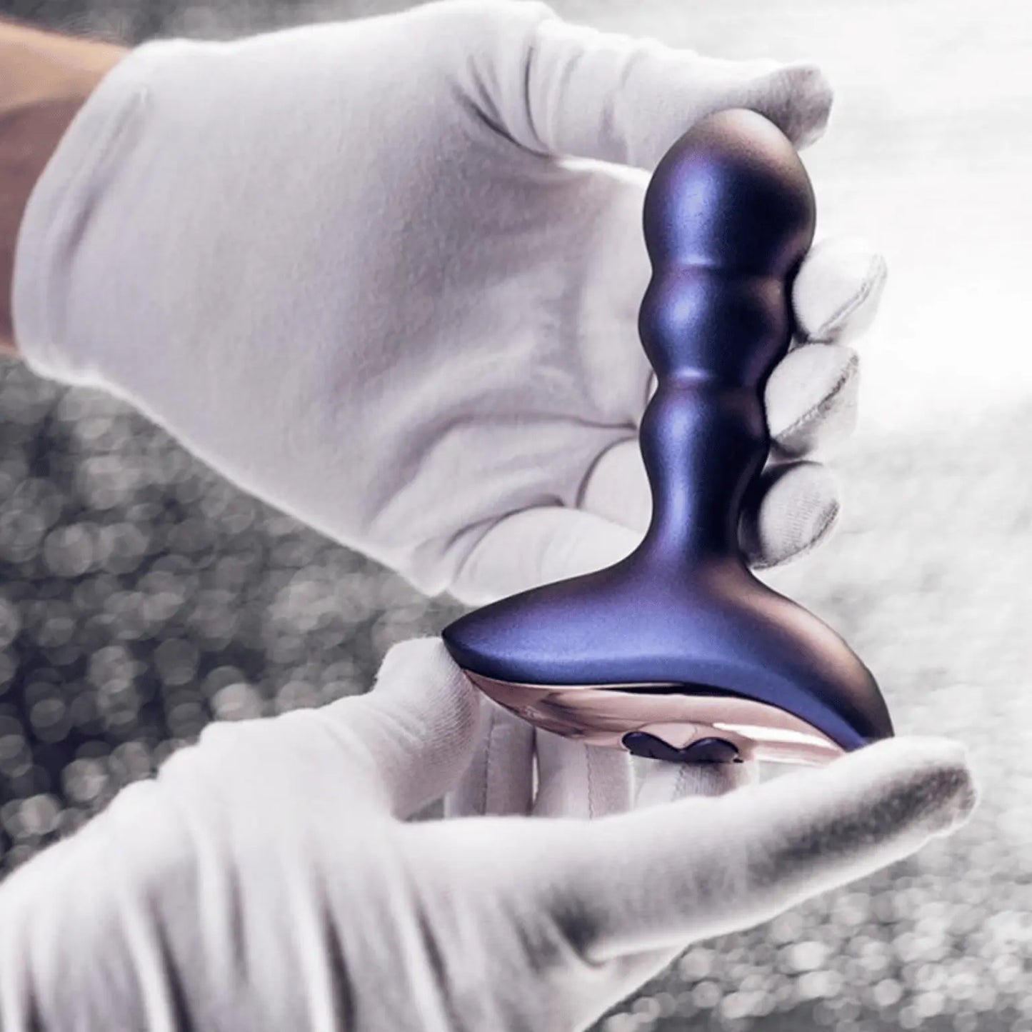 Le plug vibrant Interstellar de Hueman présenté en main avec des gants blancs, mettant en valeur son design raffiné et son ergonomie, un sextoy haut de gamme à retrouver sur Oh My God'Z.